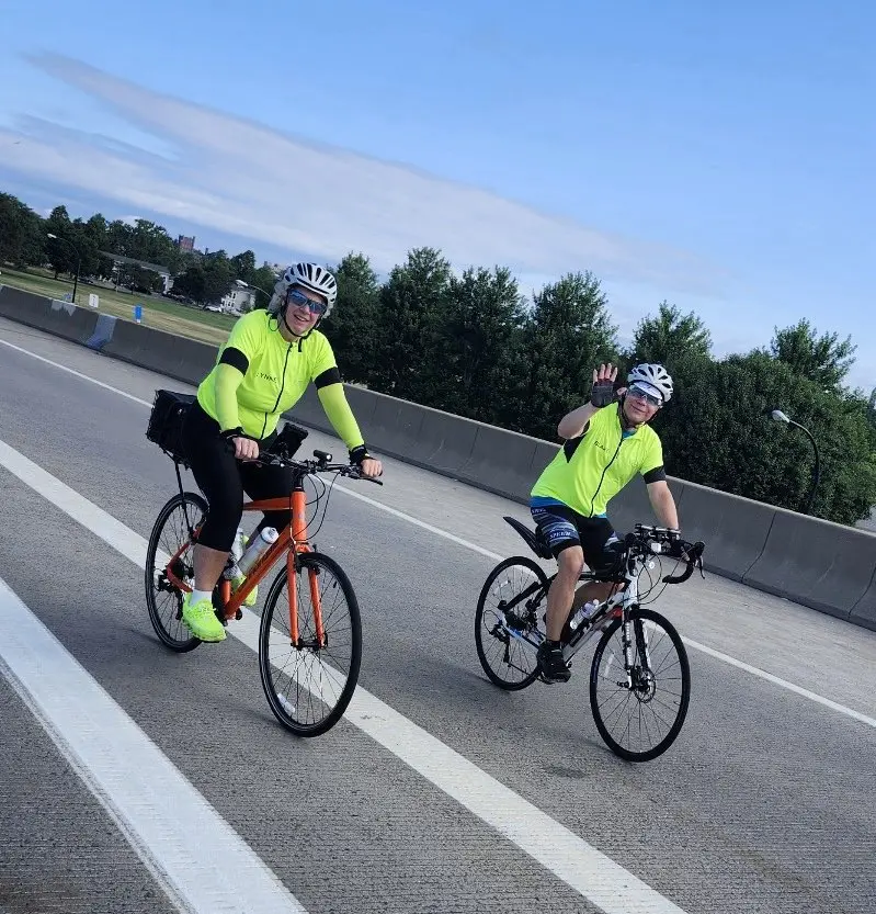 Two event marshals riding their bikes during a ride, one waves to the camera